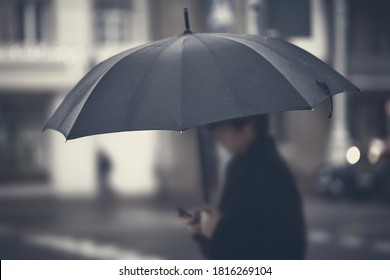 Silhouette with umbrella in rainy foggy day. Focus on umbrella, man in bokeh. Person with umbrella stands by road in rainy weather. Black umbrella, soft selective focus. - Powered by Shutterstock