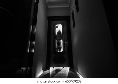 Silhouette of an unknown shadow figure with hands on a door through a closed glass door. Horror concept