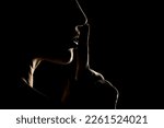 Silhouette of unknown woman with the face in the shadow holding finger on her lips on a black studio background