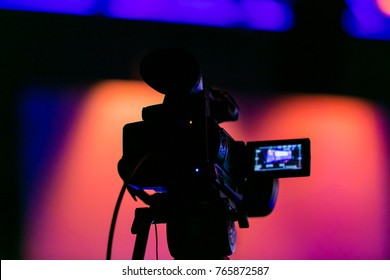 Silhouette Of A Video Camera Capturing An Event On Stage. Live Streaming Tv. Breaking News. News Event. Story. Reporter. Live Broadcast