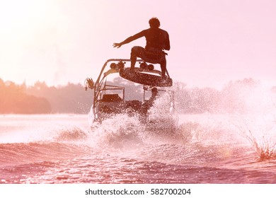 Silhouette of a wake skater as he launches off the wake behind a boat. Added lens flare and vintage filter.