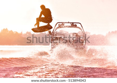 Silhouette of a wake skater as he launches off the wake behind a boat. Added lens flare and vintage filter.