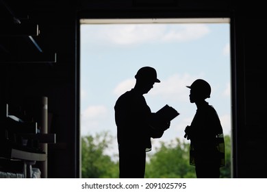 Silhouette Of Warehouse Workers Cooperating While Going Through Documents. Copy Space.