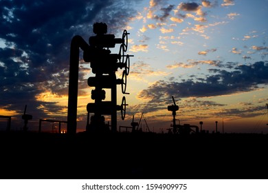 Silhouette of well head manifold in the oilfield at a cloudy sunset. 
