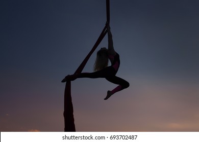 Silhouette of a woman acrobat during a show on canvases in the air.
