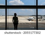 Silhouette of a woman at an airport looking out the window as a plane is docked