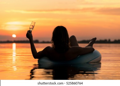 Silhouette of a woman with champagne on inflatable ring in water at sunset
