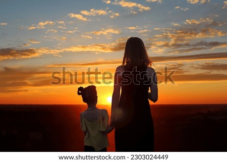 Silhouette of a woman and a child on a sunset background. A woman and a girl walk towards the sunset, view from the back.