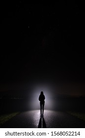 Silhouette of a woman in the darkness. Night Photography. Bright light shining behind dark mysterious figure. Ghostly, mystical, surreal person standing. - Shutterstock ID 1568052214