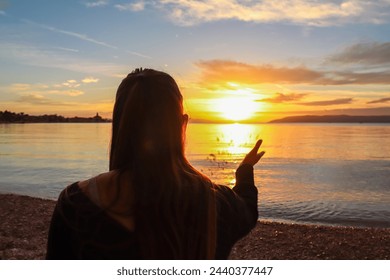 Silhouette of woman enjoying romantic sunset at beach in town Makarska, Split-Dalmatia, Croatia, Europe. Coastline of Makarska Riviera, Adriatic Sea. Dreamlike atmosphere. Travel vacation concept
