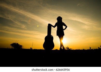 Silhouette Of Woman With Guitar Case On Sunset Background