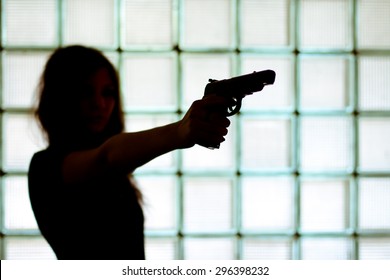 Silhouette Of A Woman With A Gun On A Glass Wall Background.