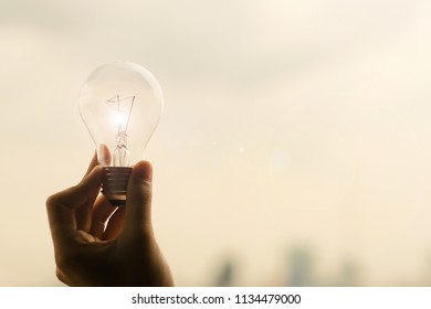 Silhouette Woman Hand Holding Light Bulb, Female Showing Lamp With Sunset Background. New Ideas, Genius And Creativity Concepts