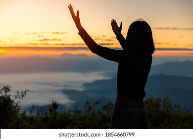 Silhouette of a woman with hands raised in the sunset concept for religion, worship, prayer and praise