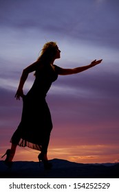 A Silhouette Of A Woman In Her Dress And High Heels Reaching Out Looking To The Side.