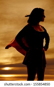 A Silhouette Of A Woman In Her Super Hero Out Fit Cape Flying.