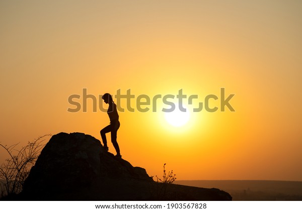 Silhouette of a woman\
hiker climbing up a big stone at sunset in mountains. Female\
tourist on high rock in evening nature. Tourism, traveling and\
healthy lifestyle\
concept.