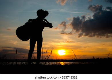 Silhouette With A Woman Holding Acoustic Guitar Case On Sunset