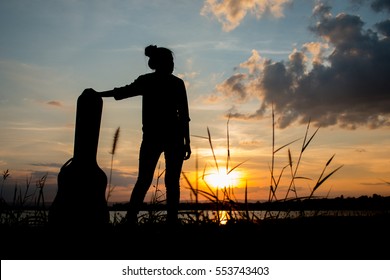 Silhouette With A Woman Holding Acoustic Guitar Case On Sunset