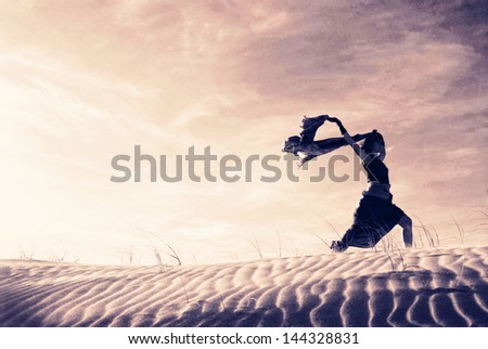 Silhouette of a woman holding a blowing scarf in the dunes.