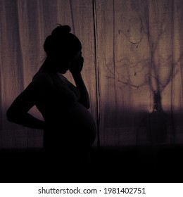 Silhouette Of A Woman Holding Her Head During Pregnancy. Pregnant Woman In Sadness At The Window