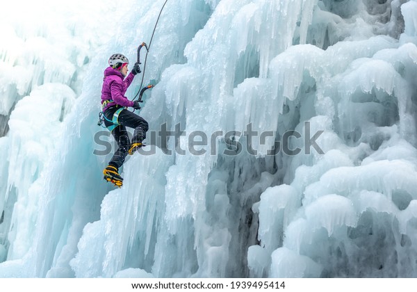 Silhouette of a woman with\
ice climbing equipment, axe and climbing rope, hiking at a frozen\
waterfall