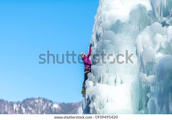 Silhouette\
of a woman with ice climbing equipment, axes and climbing ropes,\
hiking at a frozen waterfall, pulling a\
rope