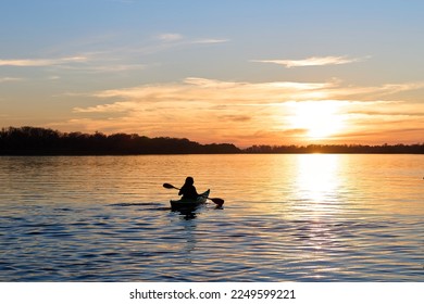 Silhouette of woman kayaking on river at golden sunset. Active recreation, healthy lifestyle and care about mental health, resting in privacy and peace