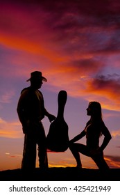 A Silhouette Of A Woman Kneeling Down In Front Of Her Cowboy, Who Is Holding On To A Guitar Case.