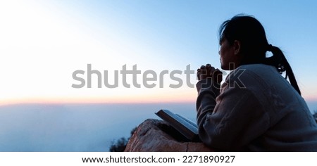 Silhouette of woman kneeling down praying for worship God at sky background. Christians pray to jesus christ for calmness. In morning people got to a quiet place and prayed. Banner with copy space.