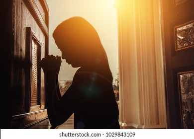 silhouette of woman kneeling and praying in modern church at sunset time