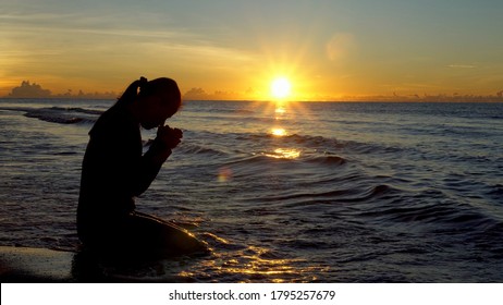 Silhouette Of Woman Kneeling And Praying Over Beautiful Sunrise At Sea Background