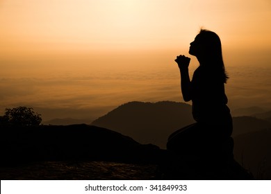 Silhouette of woman kneeling and praying over beautiful sunrise background