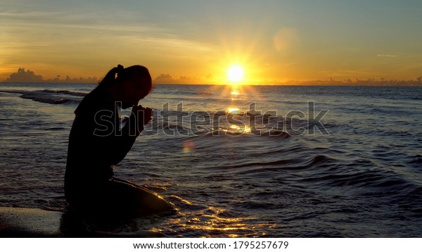 Silhouette of woman kneeling and praying over\
beautiful sunrise at sea\
background