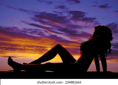 A silhouette of a woman laying back in her bikini with her face up towards the sky.
