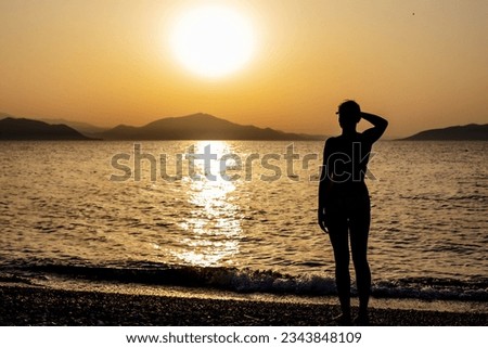 Silhouette of a woman looking far out at the bay of the sea or ocean at sunset. Loneliness, waiting for somebody.
