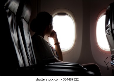 Silhouette Of Woman Looks Out The Window Of An Flying Airplane. Passenger On The Plane Resting Beside The Window. 