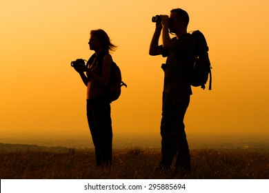 A silhouette of a woman and man with backpack looking at sunset. Couple with backpack watching the sunset
