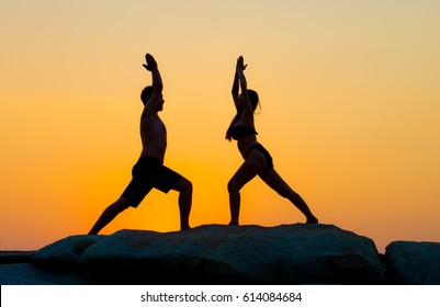 Silhouette Woman Meditating At Sunset Beach, Woman And Man Yoga Exercising Training In Serene Ocean Landscape,Thailand Scene,Couple Yoga On The Rock At The Sunset