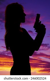 A silhouette of a woman in the outdoors holding on to a pistol.