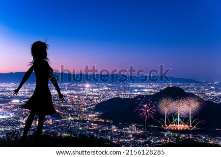 A silhouette of a woman overlooking the fireworks from the top of the mountain.