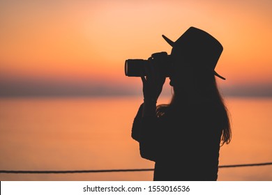 Silhouette of a woman photographer in hat with dslr camera during taking photos at sunset - Powered by Shutterstock