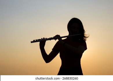 Silhouette Woman Playing Flute In Sunset Sky Background.