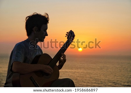 Silhouette of woman playing guitar, sunrise over sea in background
