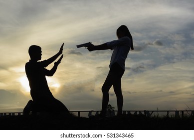 silhouette woman pointing a gun. Mafia girl shooting at someone on the sunset background.Silhouette Concept
