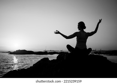 Silhouette Of A Woman Practicing Yoga During Sunset On The Sea. Black And White Photo.