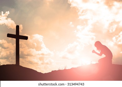 Silhouette of woman praying with cross over beautiful sky background