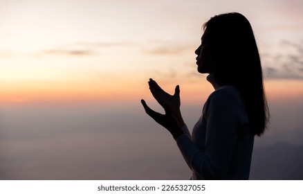  Silhouette of Woman praying for thank god praying with her hands together to think of a loving God, we praise God with light flare in the green nature. - Shutterstock ID 2265327055