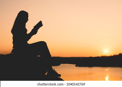 Silhouette Woman Reading A Book In Park During Sunset