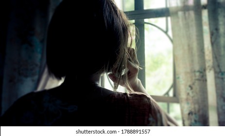 Silhouette of a woman receiving a grim call while facing the window at home. Distress, loss, or sadness concept.